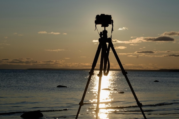 Câmera com tripé sobre o pôr do sol perto da água do mar
