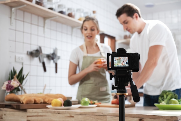 Câmera digital mirrorless profissional que grava blog de vídeo do feliz casal caucasiano cozinhando na sala da cozinha, câmera para fotógrafo ou vídeo e conceito de transmissão ao vivo, vlogger e blogueiro.