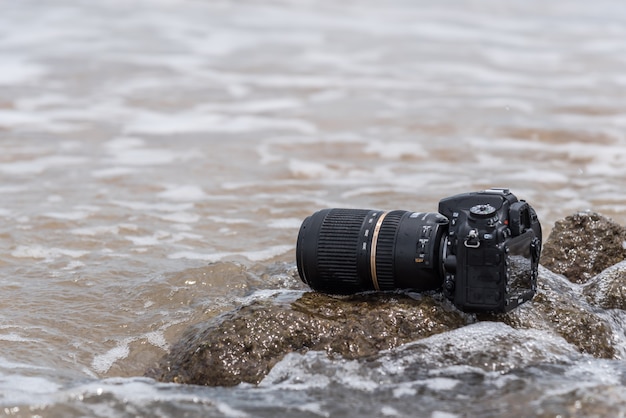 Câmera DSLR na praia molhada da onda do mar de água