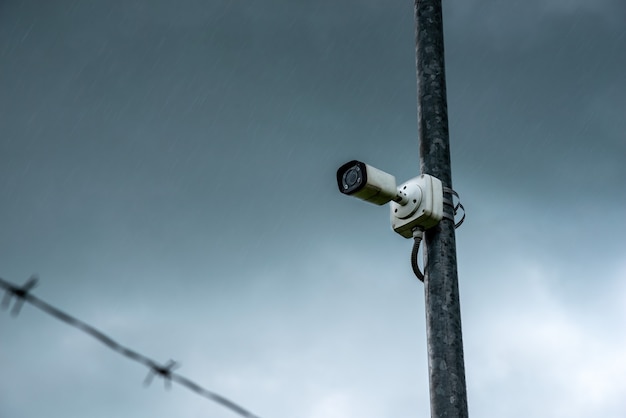 Câmera infravermelha de segurança para eventos de monitor. Câmera IP CCTV contra o fundo de céu nublado, chuva e arame farpado