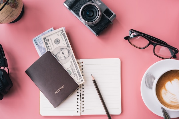 Câmera, óculos, fone de ouvido e o bloco de notas no fundo rosa, conceito de planejador de viagem.