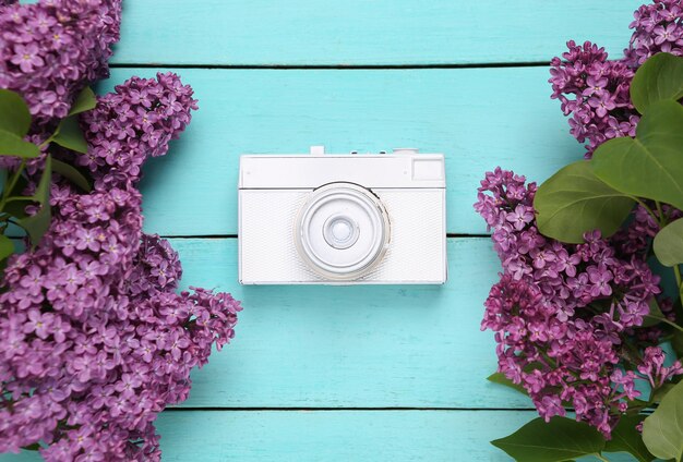 Câmera retrô com galhos de lilases florescendo em fundo azul de madeira Conceito de primavera Vista superior Flat lay