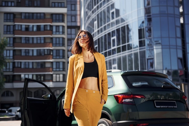 Camina hacia adelante desde el automóvil Joven mujer de moda con abrigo de color burdeos durante el día con su automóvil