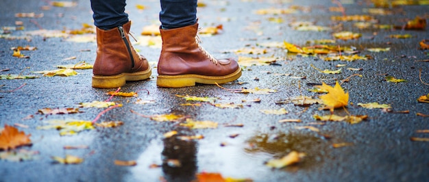 Camina sobre la acera mojada. Vista posterior en los pies de una mujer de pie sobre el pavimento de asfalto con charcos bajo la lluvia. Par de zapatos en carretera resbaladiza en el otoño. Resumen en blanco vacío del clima de otoño