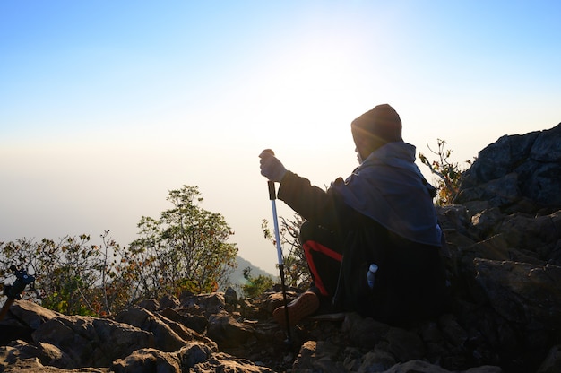 Caminando al hombre que se sienta en la colina en la montaña de la silueta de la puesta del sol con concepto de la aventura de la forma de vida del viaje.