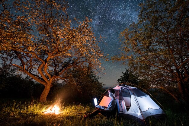 Caminante cerca de fogata y carpa turística en la noche