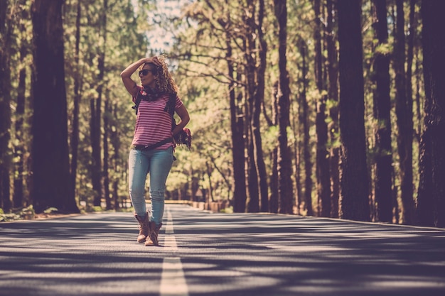 Caminante de hermosa mujer alternativa caminando en medio de la carretera en un bosque de pinos altos en el bosque para disfrutar de unas vacaciones de viaje de aventura solo en contacto y sintiéndose con la naturaleza al aire libre