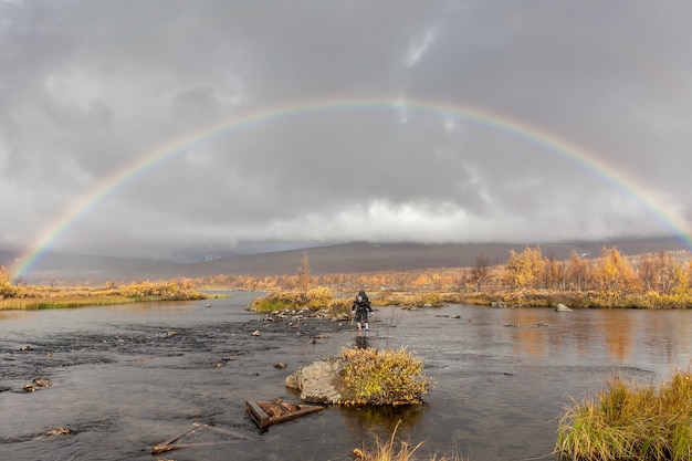 Caminante con mochila cruza arroyo frío bajo el arco iris. en un tour de trekking en Sarek