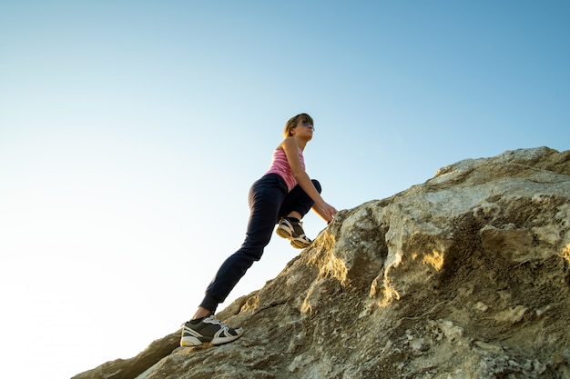 Caminante de la mujer que sube la roca grande escarpada en un día soleado. joven escaladora supera la difícil ruta de escalada. recreación activa en concepto de naturaleza.