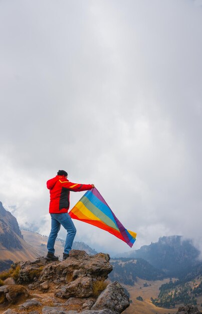 Caminante ondeando una bandera de orgullo lgbt arco iris en alta montaña. Deporte inclusivo