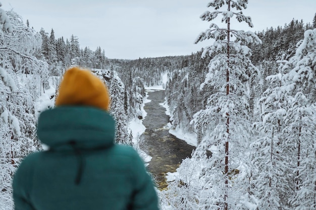 Caminante de pie junto a un río en el bosque nevado