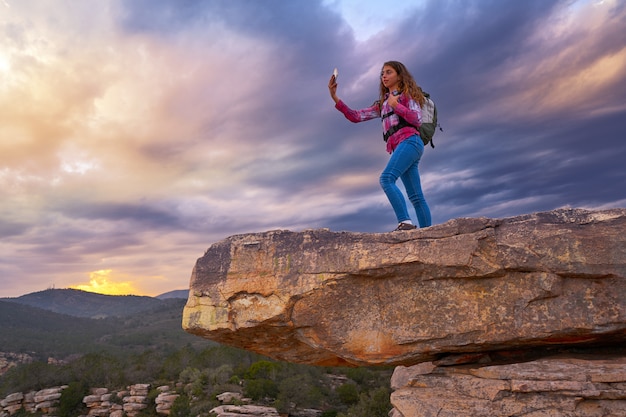 Caminante teléfono de autofoto de chica adolescente en el pico de la montaña