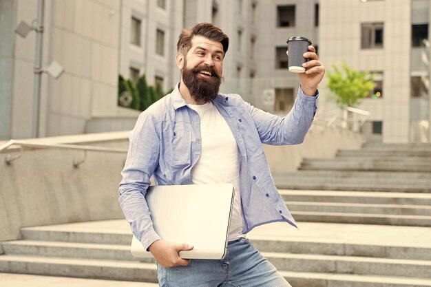 Caminaría una milla por un café Hipster feliz sosteniendo una taza de café y una computadora portátil Descanso para tomar café al aire libre Bebida caliente Café para llevar Nueva tecnología Vida moderna Desayuno matutino Experiencia rara en sabor