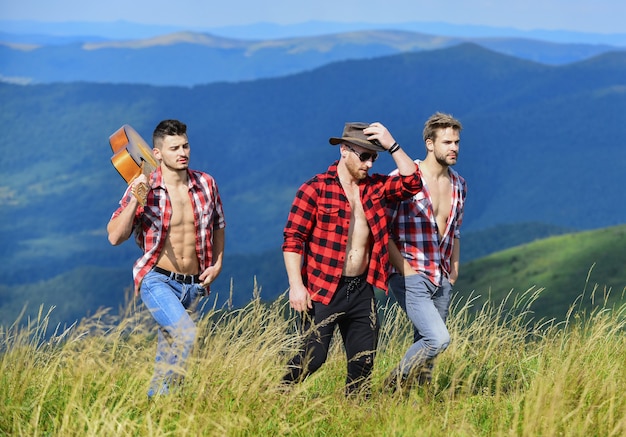 Caminata libre. grupo de personas pasan tiempo libre juntos. aventura de senderismo. hombres vaqueros. camping occidental. canciones de fogata. amigos de hombres felices con guitarra. amistad. hombres con guitarra en camisa a cuadros.