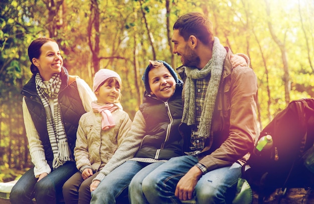 Foto caminata, viajes, turismo y concepto de personas - familia feliz sentada en un banco y hablando en el campamento en el bosque