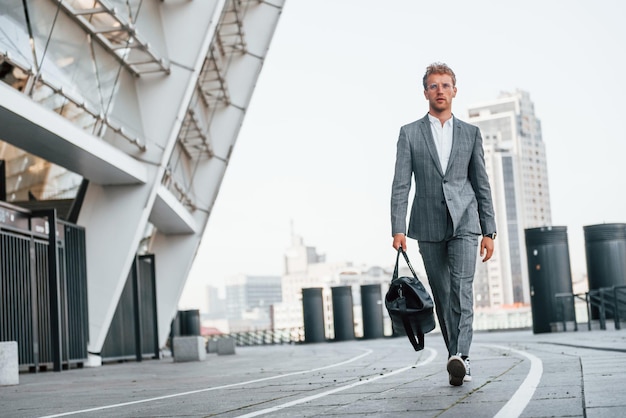 Caminha na estrada Jovem empresário com roupa formal cinza está ao ar livre na cidade