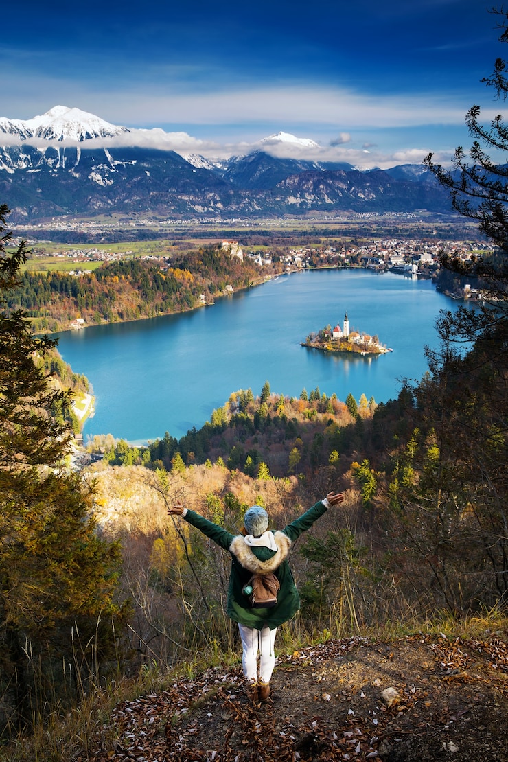Foto caminhada jovem mulher com montanhas alpes e lago alpino no fundo. viagem eslovênia, europa. vista superior na ilha com a igreja católica no lago bled com o castelo e as montanhas ao fundo.
