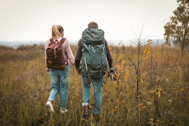 Caminhadas na natureza do outono, dois mochileiros atravessam o campo, retrovisores de homem e mulher