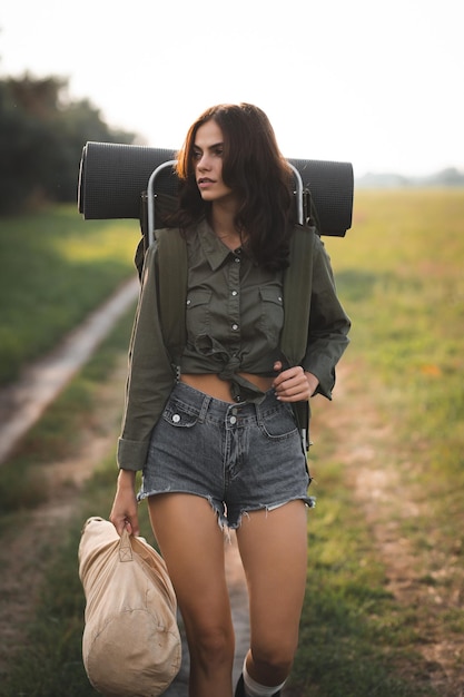 Caminhadas Uma jovem com uma mochila retrô para caminhadas caminha ao longo de uma estrada de limpeza Pedindo carona