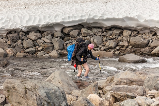 Caminhante com mochila atravessa o riacho frio. em uma excursão de trekking em Sarek