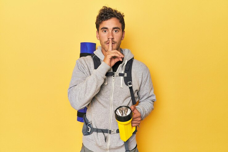 Foto caminhante com mochila e lanterna amarela guardando segredo ou pedindo silêncio