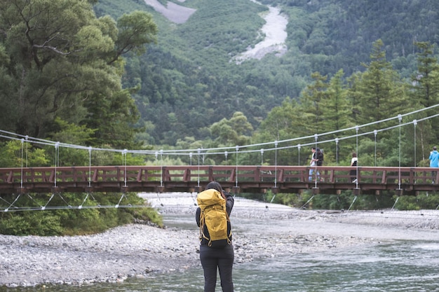 Caminhante com mochilas com ponte Kappa Kamikochi com rio e fundo de montanha Okuhotaka dake Kamikochi Lugar famoso para trekking e caminhadas em Matsumoto Nagano Japão