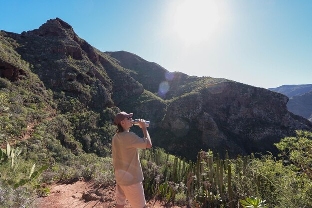 Caminhante hidratando-se em meio a montanhas majestosas capturadas em uma moldura horizontal com o sol brilhando de t