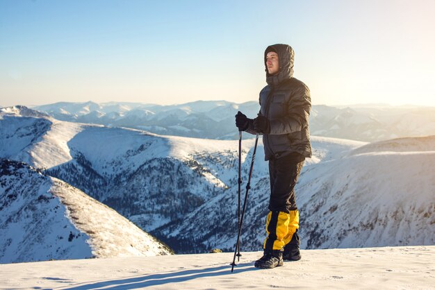 Caminhantes do homem em pé no pico da montanha de neve ao pôr do sol