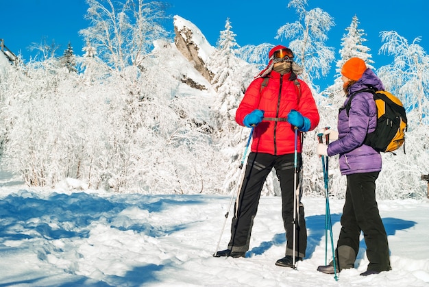 Caminhantes homem e mulher com mochilas e bastões de caminhada nórdica em uma paisagem gelada de inverno