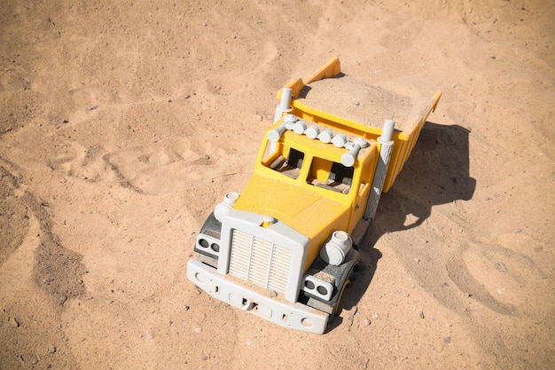 Caminhão de brinquedo amarelo na areia em um dia ensolarado