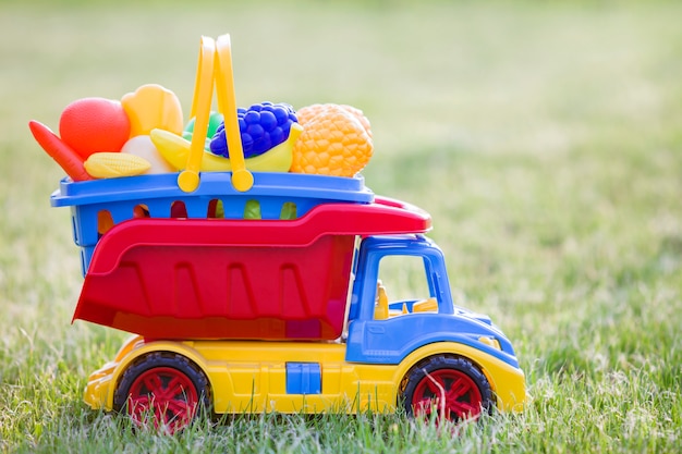 Caminhão de carro de brinquedo colorido plástico brilhante carregando cesta com frutas e legumes de brinquedo ao ar livre