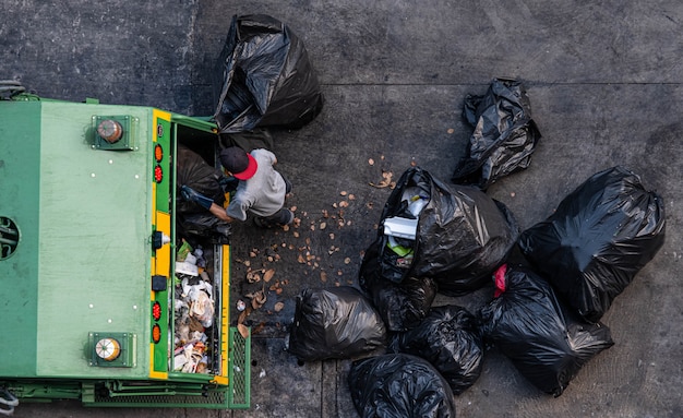 Caminhão de lixo verde e os funcionários estão coletando muitos sacos de lixo pretos