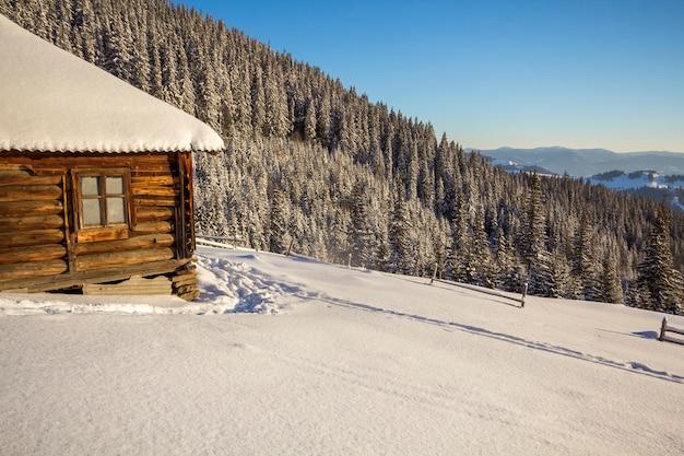 Caminho da pegada humana na neve profunda branca, levando a pequena cabana de pastor abandonada de madeira velha no vale da montanha