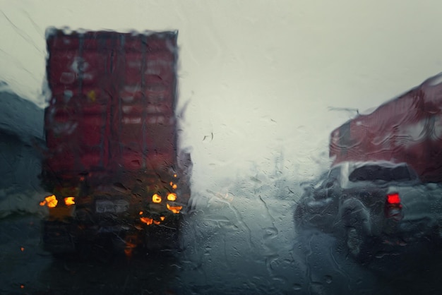 Caminhões embaçados veem através do para-brisa de um carro na chuva Foco seletivo e tons de cor