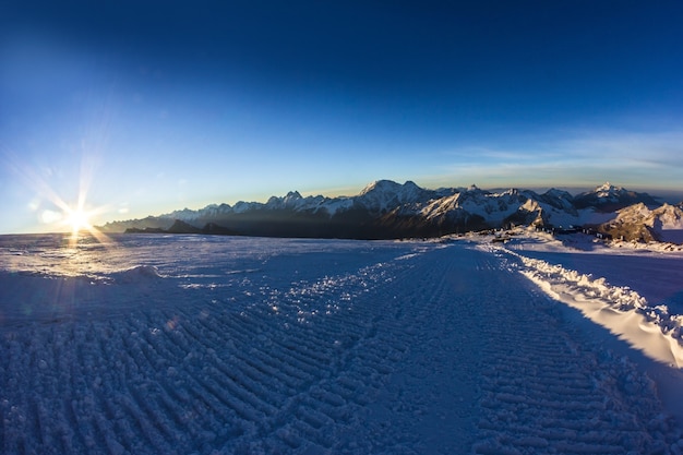 Camino ancho desde el snowcat y la cordillera en los rayos del sol naciente