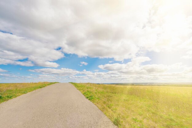 Camino asfaltado a través del campo con hierba verde bajo un cielo azul con nubes