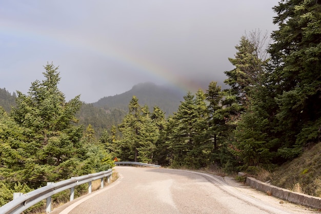 Camino en el campo y un arco iris sobre las montañas y la montaña del bosque Nafpaktia Grecia occidental