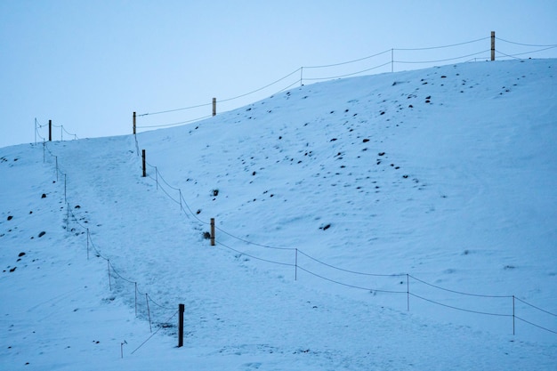 Camino cuesta arriba cercado por una colina totalmente cubierta de nieve justo al lado de una playa negra totalmente cubierta de nieve