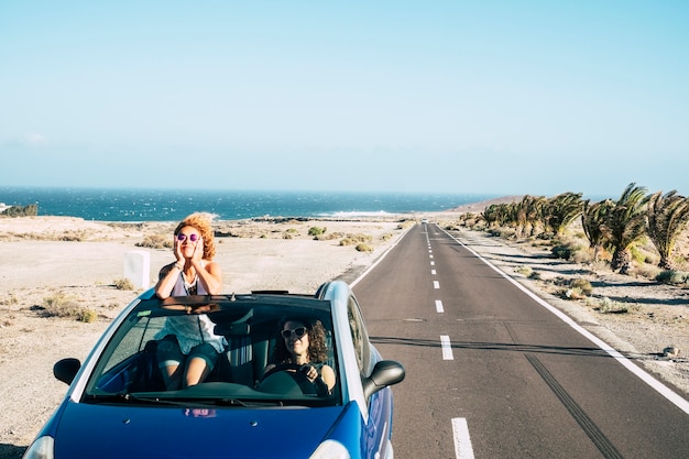 Camino largo y amigos viajan juntos en concepto de libertad e independencia con un par de mujeres jóvenes que conducen de vacaciones