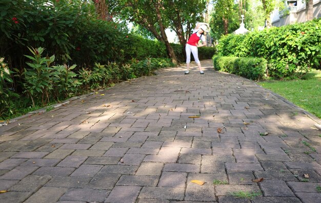 Camino de pavimentación en un jardín de verano con una mujer en ejercicio borrosa en la lejanía