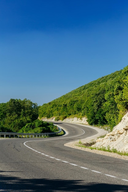 Camino pavimentado con curvas huyendo entre montañas rocosas con árboles verdes