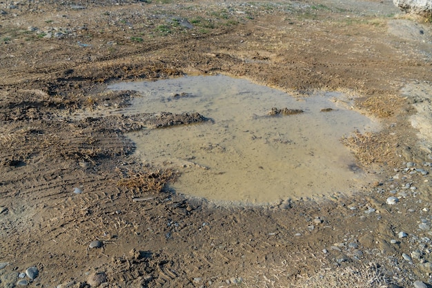 Un camino de ripio mojado lleno de baches después de la textura de la lluvia