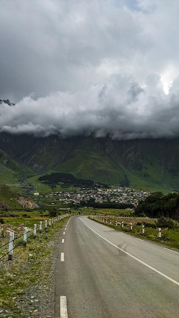 Camino solitario al pueblo y montañas bajo espesas nubes en verano.