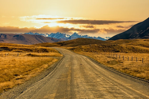 Camino de tierra de grava vacía sinuoso a través de la campiña rural del parque de conservación Hakatere en las tierras altas de Ashburton con un telón de fondo de los Alpes del Sur