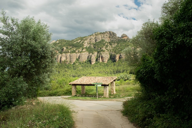 Camino a través de la zona agrícola que conduce a una cabaña techada con montañas al fondo y nublado s