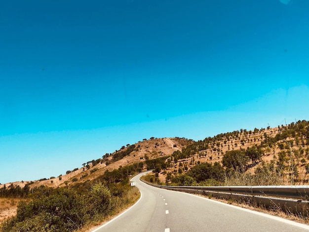 Foto camino vacío en medio de las montañas contra un cielo azul claro