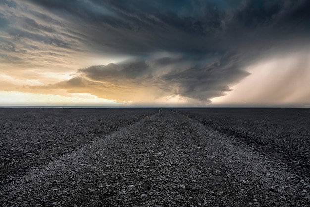 Camino vacío sobre arena de lava en la playa negra contra el cielo dramático durante la puesta de sol