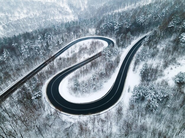 Camino ventoso con curvas en un bosque cubierto de nieve Vista aérea de drones de arriba hacia abajo ViewxA
