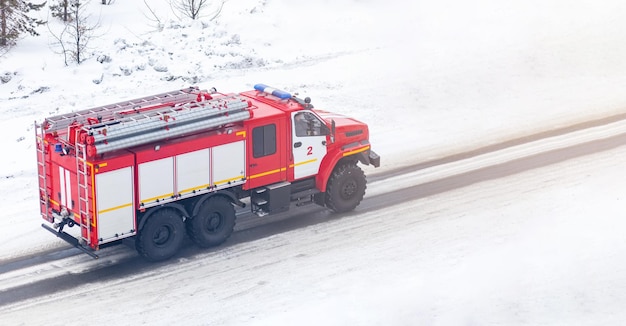 Un camión de bomberos rojo o un camión de bomberos conduce por una calle nevada en invierno