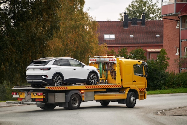 Un camión de remolque lleva un coche en un remolque de cama plana en la carretera proporcionando servicio de transporte y asistencia después de un accidente